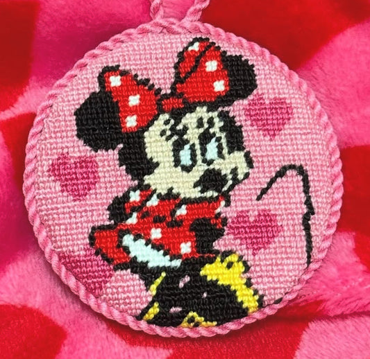 Circular needlepoint pendant with iconic girly mouse character on a pink heart-patterned fabric background